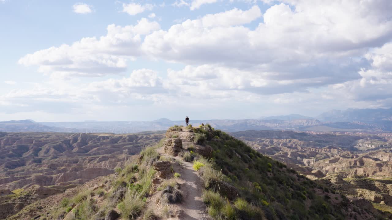 Hiker walking on trail with wide scenic view of rugged hill landscape