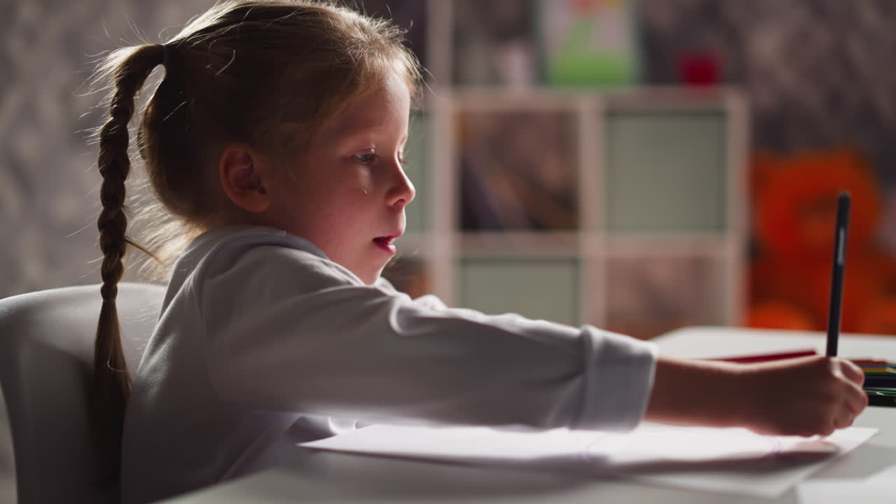 Una bambina bionda assorta nel disegnare con i colori al tavolo.