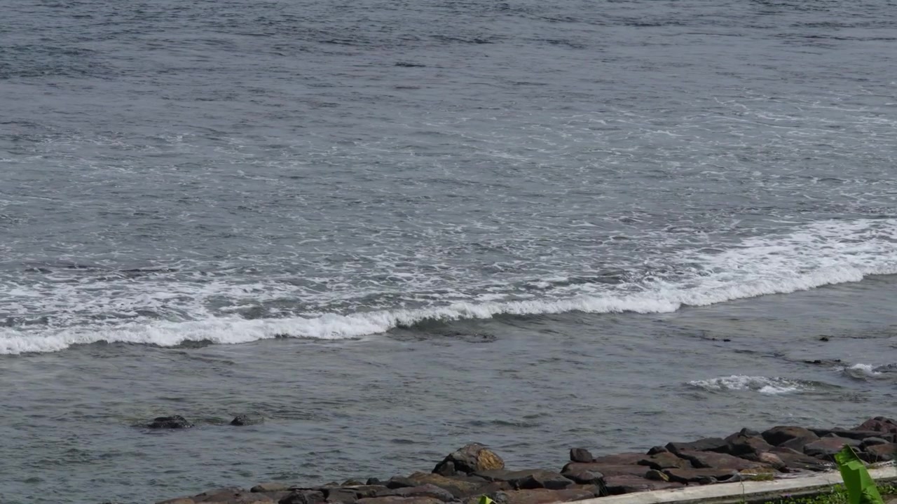 Dolci onde oceaniche si infrangono verso una costa rocciosa in una giornata nuvolosa, scena costiera.