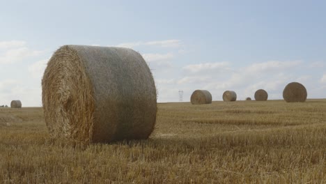 Time-lapse-of-clouds-passing-in-blue-sky-behind-large-round-hay-bales-spread-across-landscape