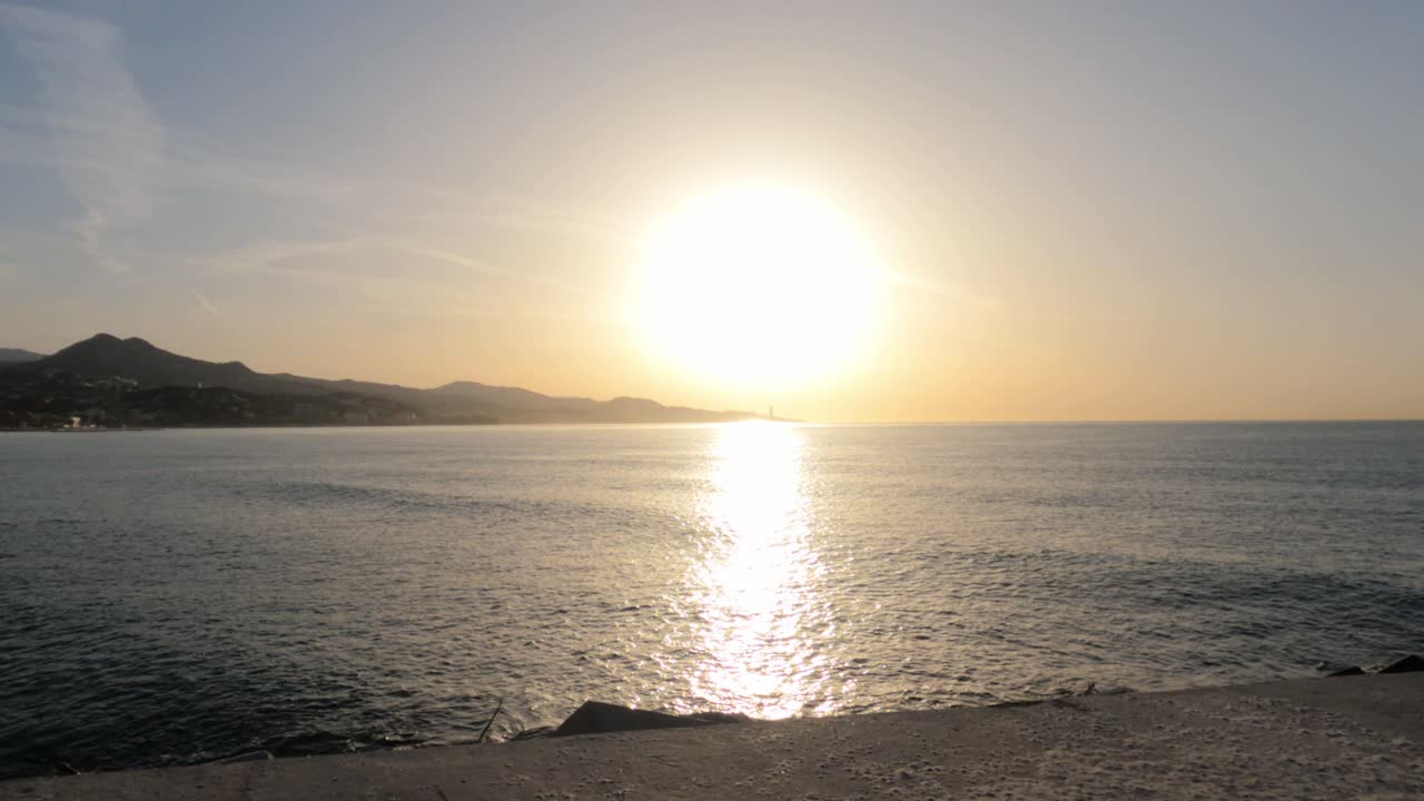 Betagende gylden solnedgang, der spejler sig i det rolige Middelhav langs Malagas kystlinje, med silhuetter af bjerge og en varmt glødende himmel