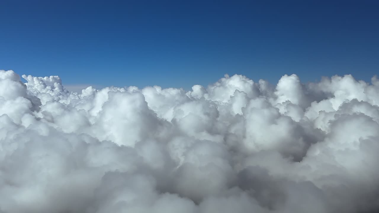 A peaceful flight experience like floating above an endless layer of cottony clouds with a deep and bright blue sky.. Aerial jet airplane cockpit view. Ultra-realistic 4K shot
