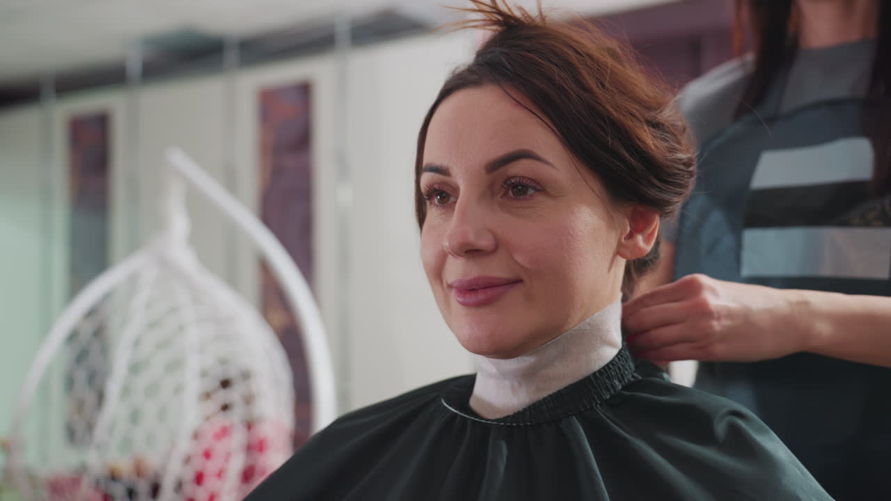 assistente che sistema un mantello a una cliente in modo professionale, assistente di bellezza che copre attentamente la cliente con un mantello prima di iniziare il taglio, stilista che si assicura che la cliente sia protetta con mantello e protezione per il collo prima della messa in piega