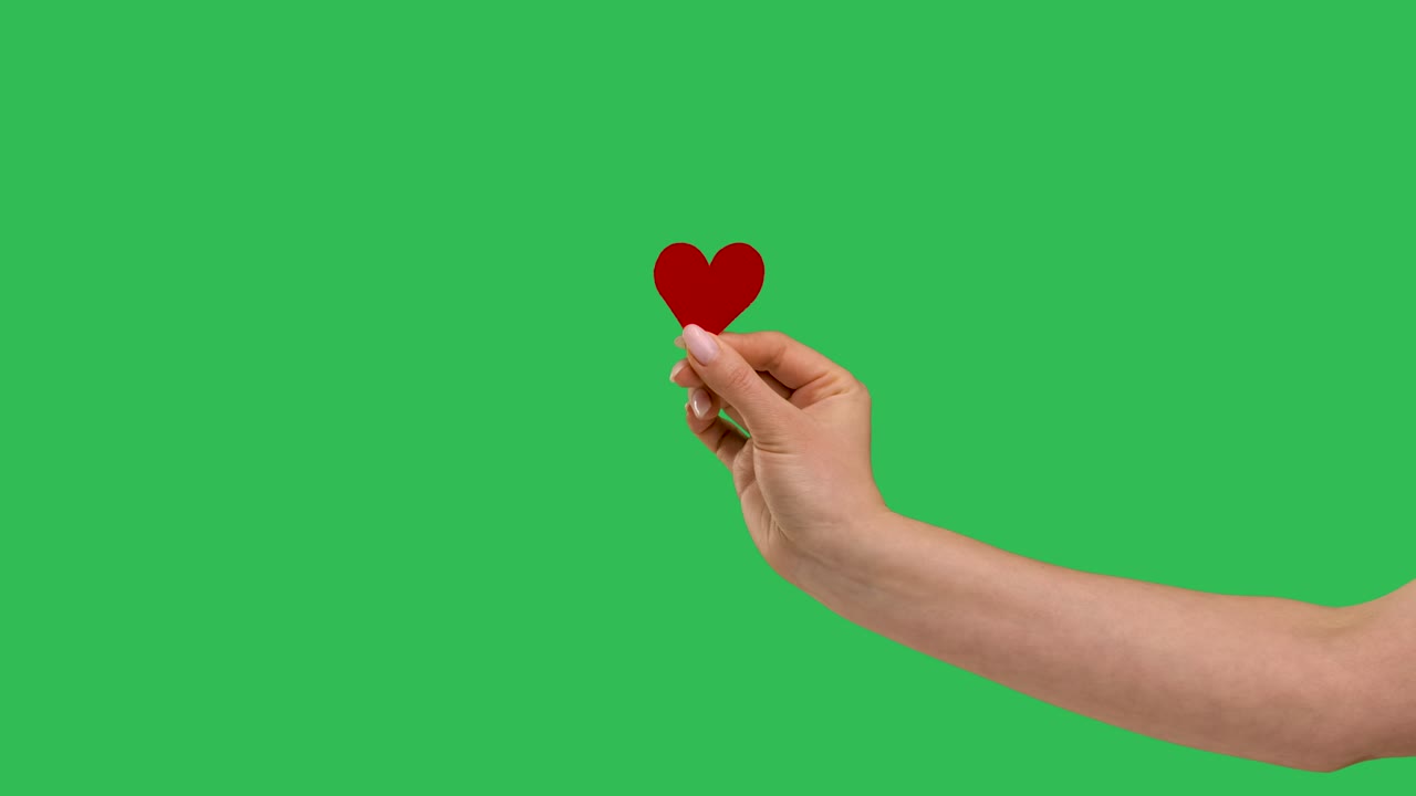 여성 블로거는 소셜 네트워크에서처럼 녹색 화면에 작은 빨간 심장을 손에 들고 있습니다. 발렌타인 데이, 국제 여성의 날, 사랑. 느린 모션.