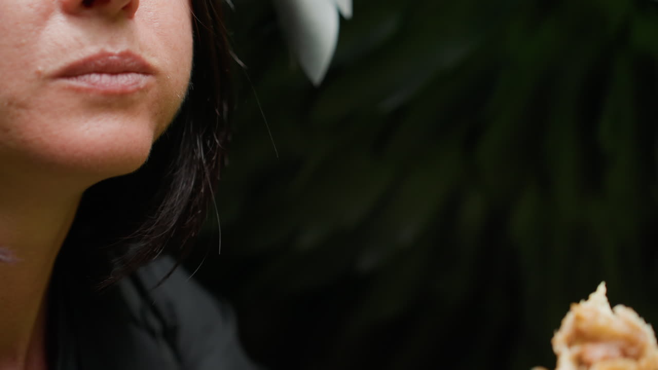 Close up of woman biting flaky pastry outdoors, hand holding golden crust delicately against soft natural background, capturing detailed texture, taste moment, and sensory emotion