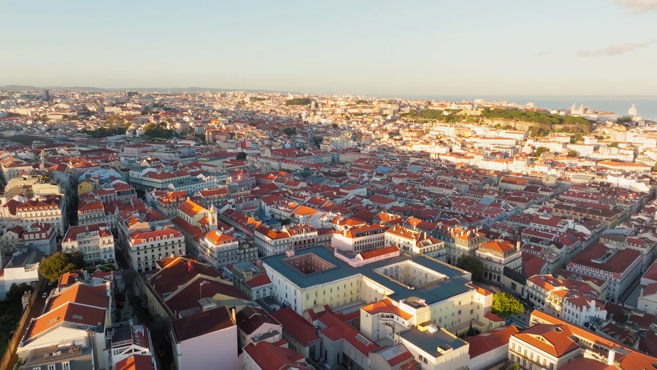 Una vista aerea mostra Lisbona, Portogallo, che risplende nella calda luce del tramonto, con fitti quartieri storici, tetti rossi, eleganti isolati cittadini e il più ampio paesaggio urbano che si estende verso l'orizzonte