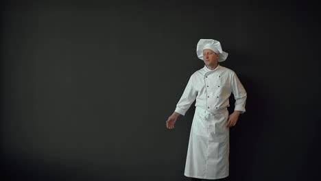 chef masculino con la mano a un lado, mostrando un espacio vacío en su palma para publicidad o texto comercial, sonriendo y mirando a la cámara. espacio de copia y fondo negro.