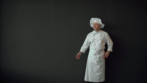 male chef with hand aside, showing an empty space on his palm for advertising or commercial text, smiling and looking at camera. copy space and black background.