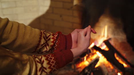 Male is warming hands near the bonfire at the twilight's inside. Fireplace in a house. Cold season concept.