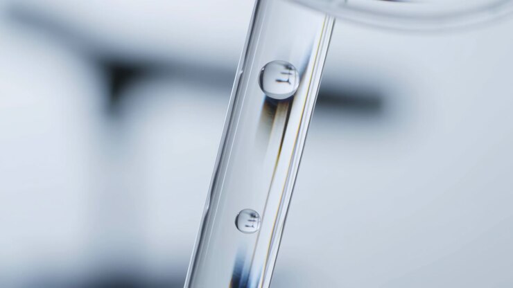 Macro close-up of a transparent glass pipette or tube holding clear liquid with tiny bubbles, shown against a softly blurred laboratory background with cool