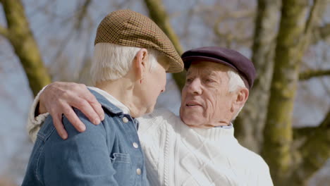 senior couple talking and kissing while sitting on bench and spending time in park on sunny autumn day 1