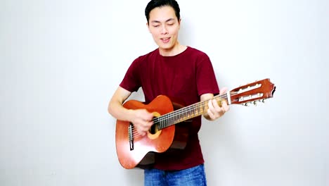 chico asiático tocando una canción feliz con su vieja guitarra acústica