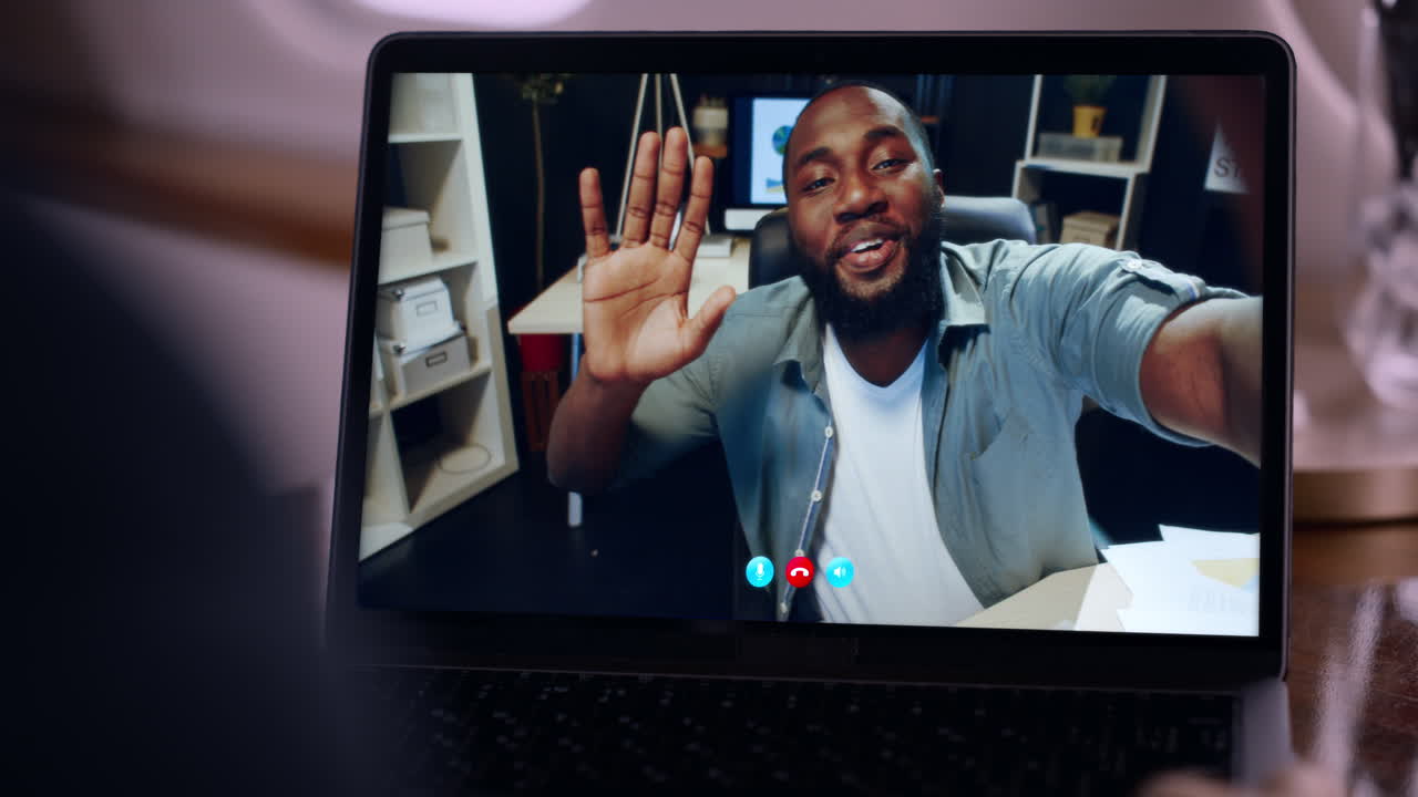Smiling man videocalling friend waving hand to laptop web camera close up
