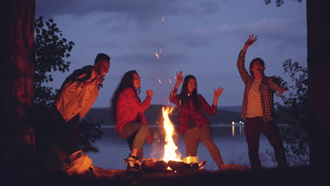 friends dancing around campfire at night