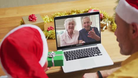 Kaukasischer-Vater-Und-Sohn-Mit-Weihnachtsmützen-Nutzen-Laptop-Für-Weihnachtsvideoanruf-Mit-Der-Familie-Auf-Dem-Bildschirm