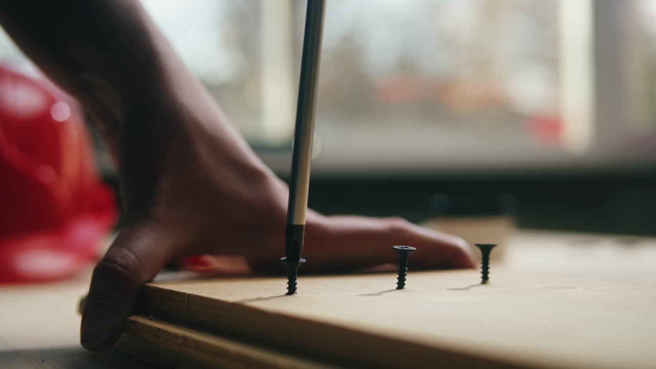 Close-up of Hand Using Screwdriver to Fasten Screw into Wooden Plank