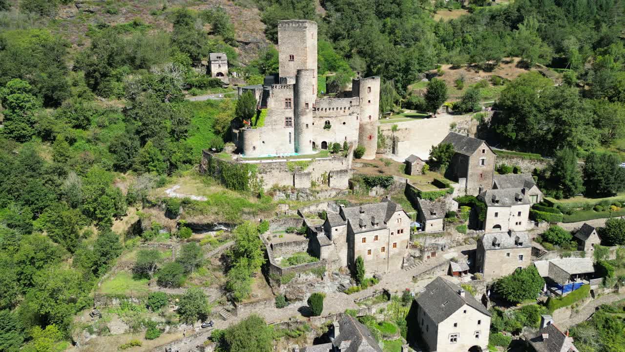 Drone aerial view in France countryside small old medieval brick town and a castle on a green mountain forest flying around on a sunny day in Belcastel