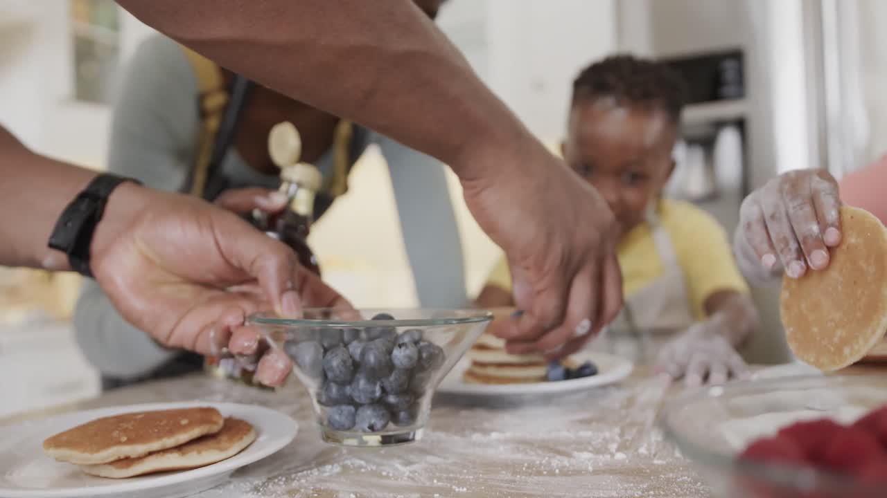 Happy african american couple with son and daughter serving pancakes in kitchen, slow motion