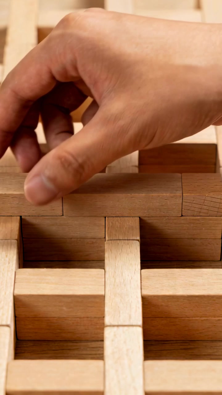 Video verticale: Una mano destra si avvicina e spinge un piccolo blocco fuori da una griglia di legno su un tavolo, creando un vuoto.