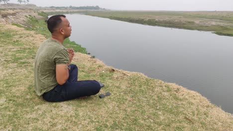 back of a boy sitting in lotus pose in front of the sea practicing yoga and praying in an open field on a summer morning