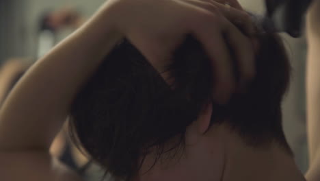 close up over the shoulder shot of woman blowdrying and brushing her hair while looking in the mirror