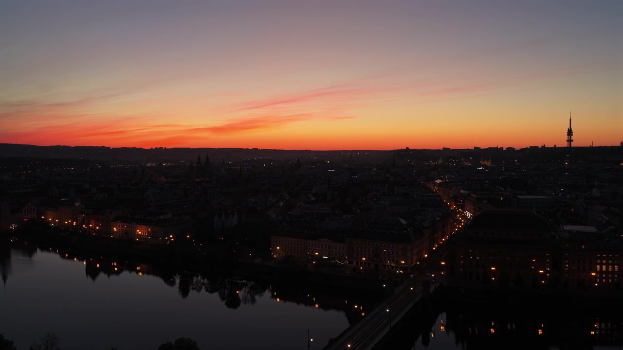 Aerial drone view of Prague city skyline at sunset with the Vltava river and Zizkov television tower silhouetted against a vivid red and orange sky, Prague, Czech Republic.