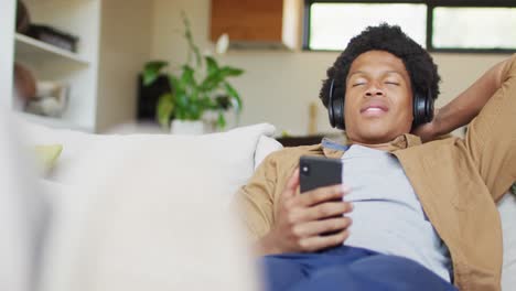 Glücklicher-Afroamerikanischer-Mann,-Der-Zu-Hause-Smartphone-Und-Kopfhörer-Benutzt