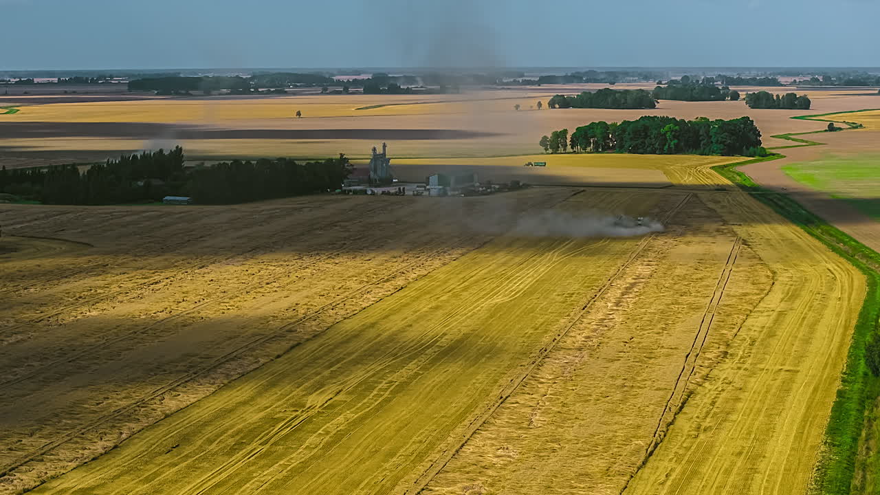 Timelapse of hay combine harvester gathering grain and clearing fields, smoke rises from behind