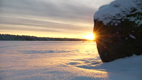 Sunset-with-snow-landscape-during-winter-solstice,-Reveal-shot-behind-stone