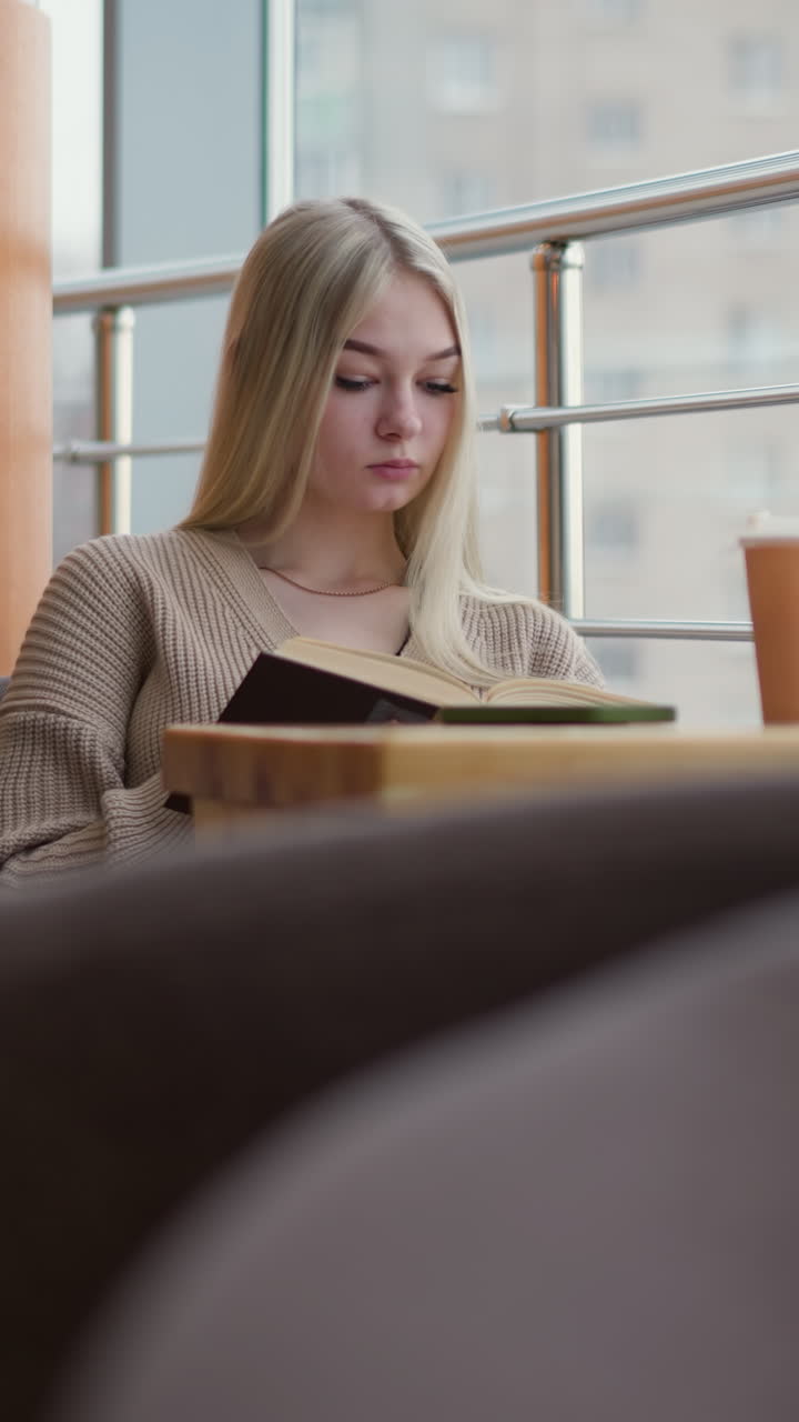 Karrierekvinne sitter på en moderne kafé og leser en bok med et fokusert uttrykk. En kaffekopp står på bordet, og store vinduer gir naturlig lys. Hun er tankefull og fordypet i lesingen.