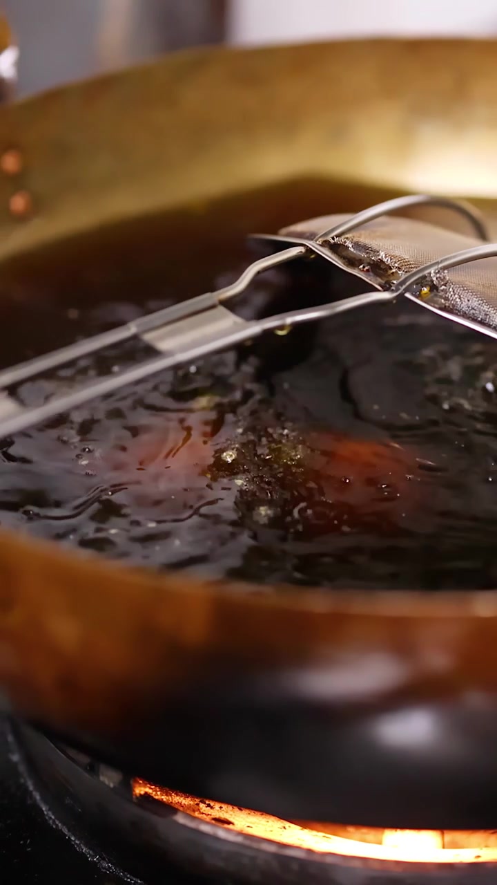 Close-up of samosas frying in hot oil within a brass wok on a Bangkok street.
