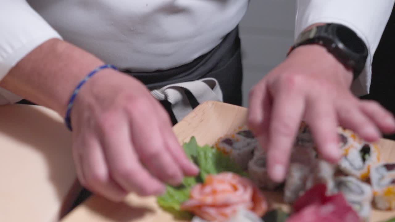 A roaming shot follows from a sushi chef’s face to him placing sushi rolls onto a decorative board, showcasing the precision and artistry of sushi presentation. Ideal for culinary and sushi content.