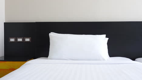 tilt down shot of a clean hotel bed with pristine white pillows and clean white sheets and a subtle grey stripe against a black headboard