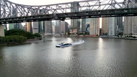 Volando-Bajo-El-Puente-Story-Con-Un-Ferry-Citycat-Viajando-Por-El-Río-Brisbane-En-Queensland,-Australia