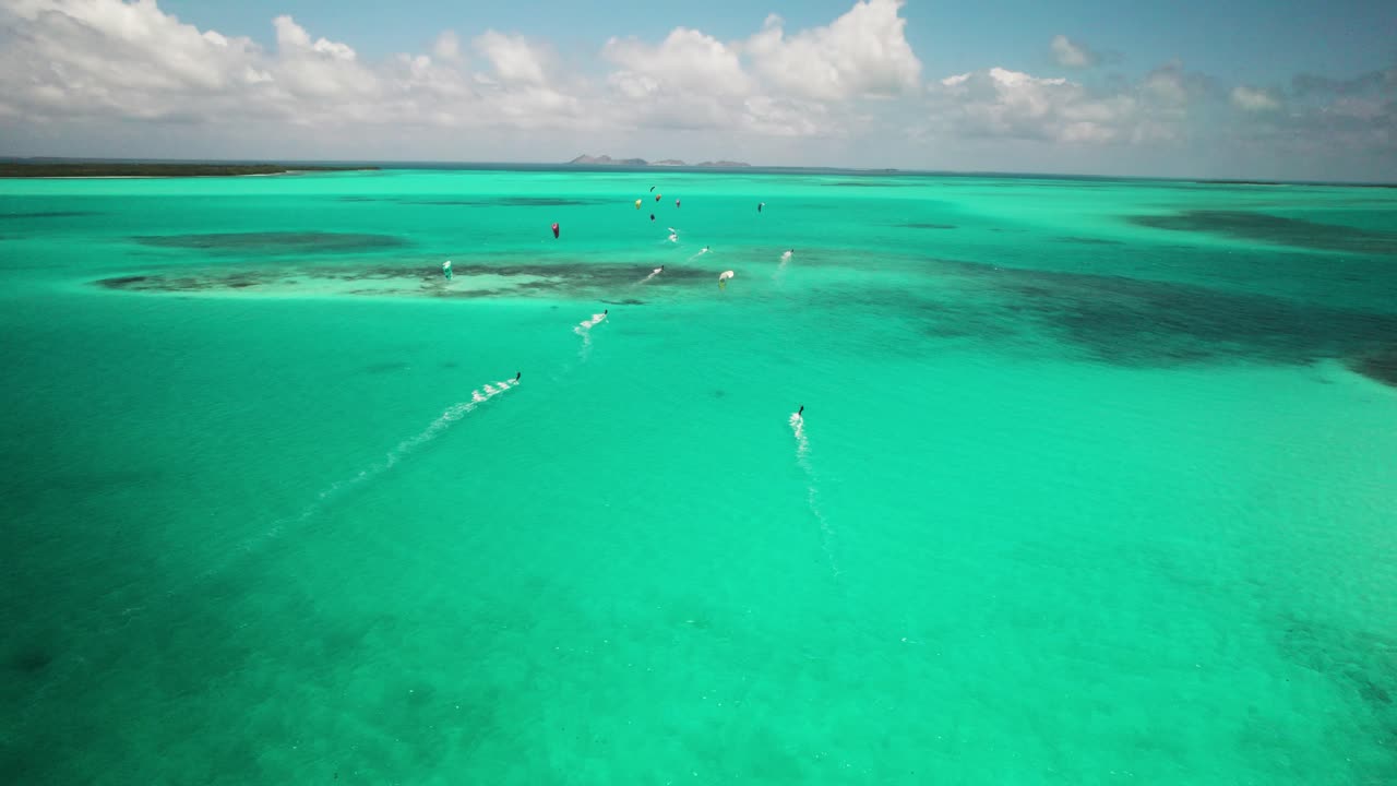Kitesurfers glide across vibrant turquoise waters under a sunny sky