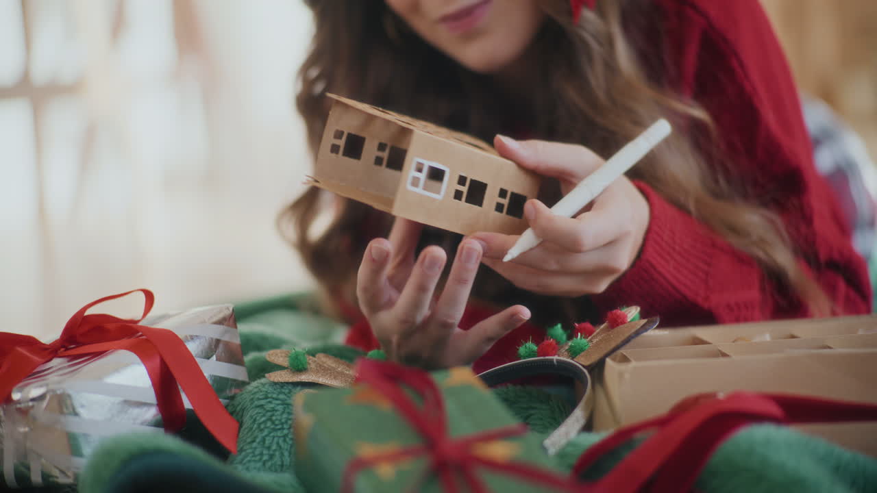 mujer recortada coloreando cartón ornamento de la casa durante la navidad