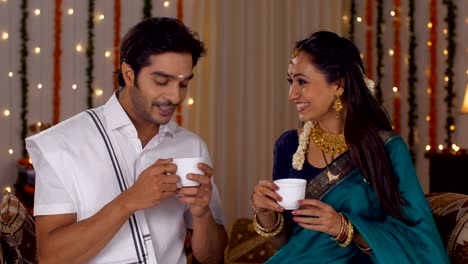 south indian couple dressed in a traditional dress and drinking a hot tea together - lifestyle
