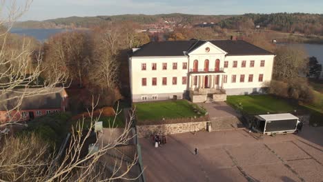 Drone-descending-near-large-white-lakeside-mansion-house-in-autumn