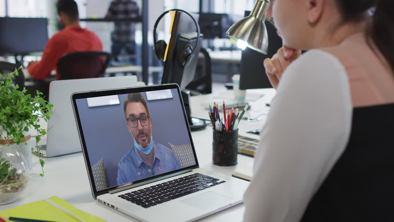 Caucasian woman having a video call with male office colleague on laptop at office