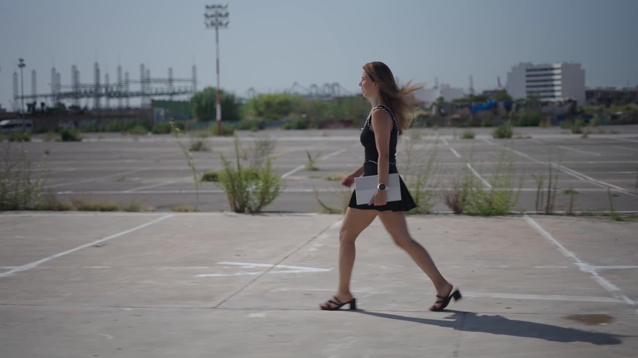Woman Walking with Laptop in Urban Parking Lot
