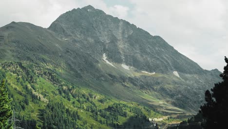 steep rocky alpine mountain top with snow and tree covered land n a cloudy summer day