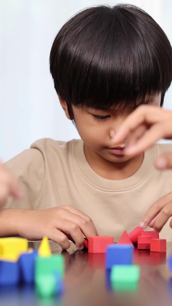 Un giovane ragazzo asiatico e adulti che costruiscono insieme blocchi di plastica colorati a casa, alla luce naturale.