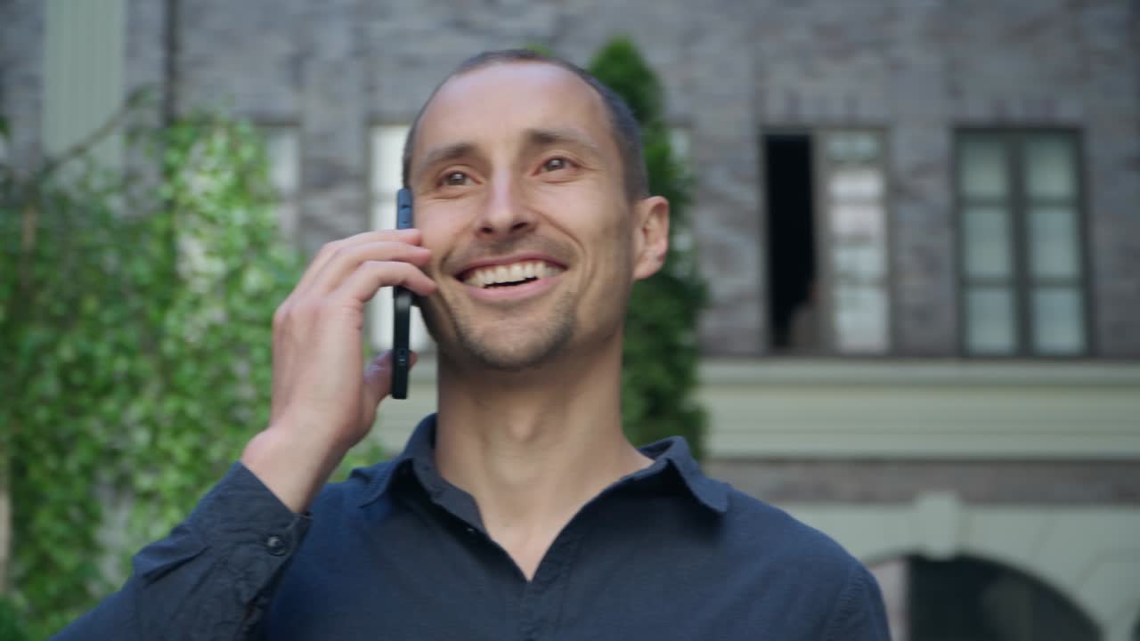hombre joven de 4k de pie en la calle en el fondo de un edificio moderno hablando por teléfono