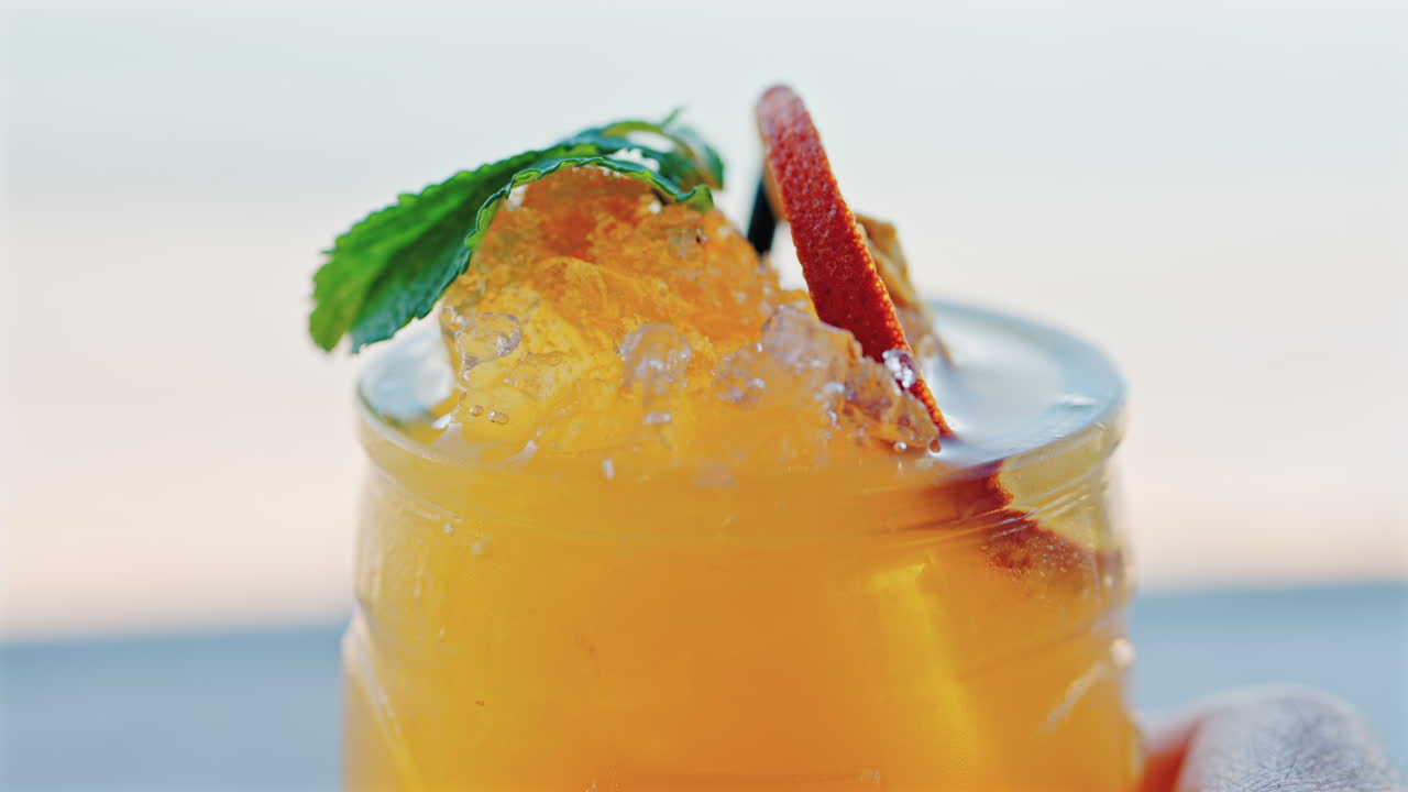 Close up of an orange cocktail on a table with a blurred view of the sea on the background