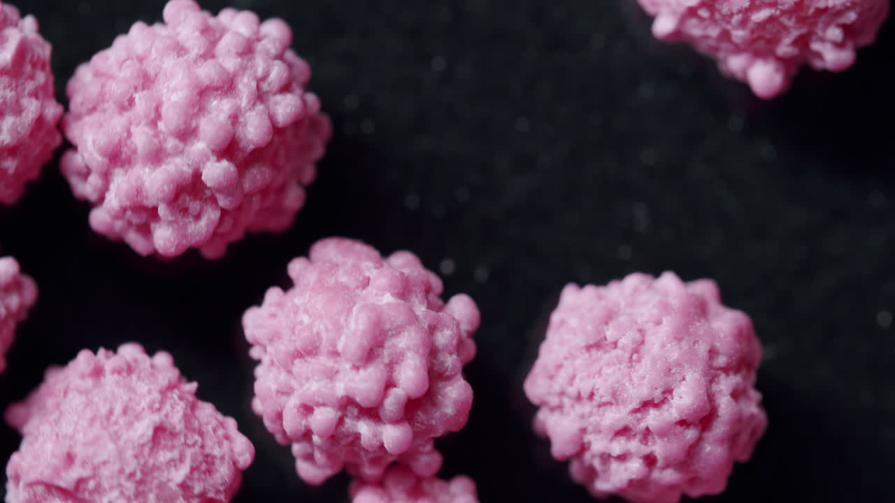 Top shot of pink particles spinning clockwise on a dark surface. Commercial side light from the left. Particles looking like a virus or disease. Virus cells moving and shaking