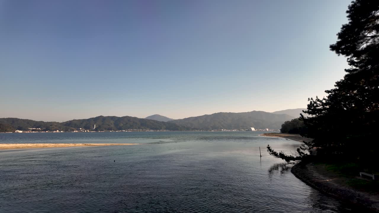 Scenic view of the Amanohashidate sandbar, a natural wonder forming a bridge between Miyazu Bay and the Aso Sea, with mountains and clear sky in the background