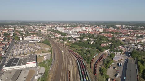 aerial view of a city's railway hub with multiple train tracks converging near the urban center. passenger and freight trains can be seen traveling and parked, surrounded by residential buildings.