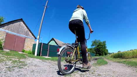 una mujer joven montando una bicicleta de época a lo largo de una carretera rural en un pueblo