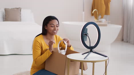 woman unboxing headphones and showing them to her audience via online streaming.