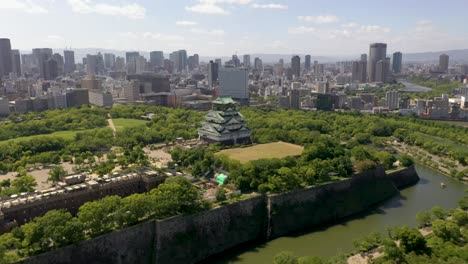 Aerial-of-famous-landmark-Osaka-Castle-with-park,-moat,-skyscraper,-and-city-in-Osaka,-Japan